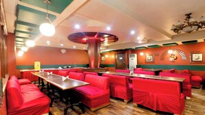 Un restaurant avec des banquettes et des tables recouvertes d’un tissu rouge, une colonne décorative centrale et un plancher en bois.