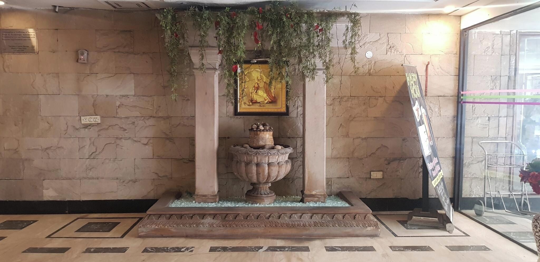 A reception area with a marble floor, a large decorative urn, and a framed picture above it.