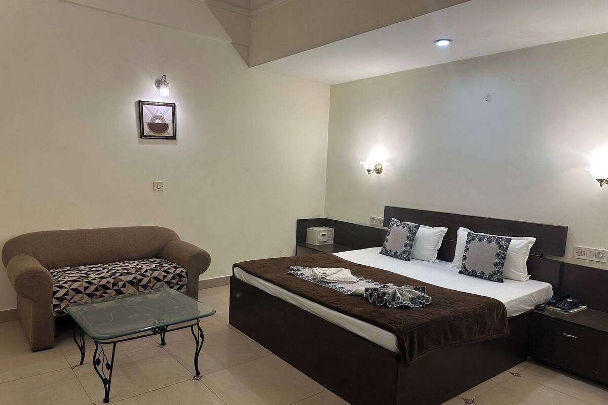 Un dormitorio con una cama grande, un sofá, una mesita y dos luces fijadas a la pared.