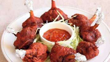 A plate of tandoori chicken legs with foil-wrapped ends, served with a side of sauce and garnished with greens.