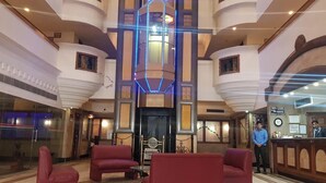 Un hall d'hôtel doté d'un grand lustre central, d'un espace salon et d'un comptoir d'accueil.