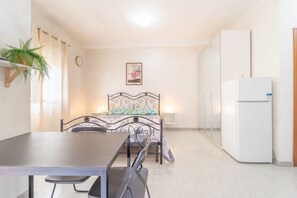 A small, well-lit room with a bed, a table, chairs, a refrigerator, and a potted plant. - Anagnina residence, 400m from Metro A (Roma)