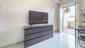 A modern room with a flat-screen TV on a dark dresser, a sliding glass door leading to an outdoor area, and a small table with a chair. - Anagnina residence, 400m from Metro A (Roma)