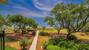 A pathway leading through a landscaped garden with mature trees and a clear sky.