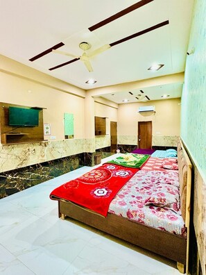 A bedroom with a bed, a ceiling fan, a TV, and a marble wall. - RAGHAV DHAM (Vrindavan)