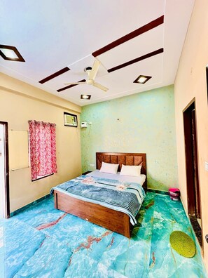 A bedroom with a bed, a ceiling fan, and a wall-mounted air conditioner. - RAGHAV DHAM (Vrindavan)