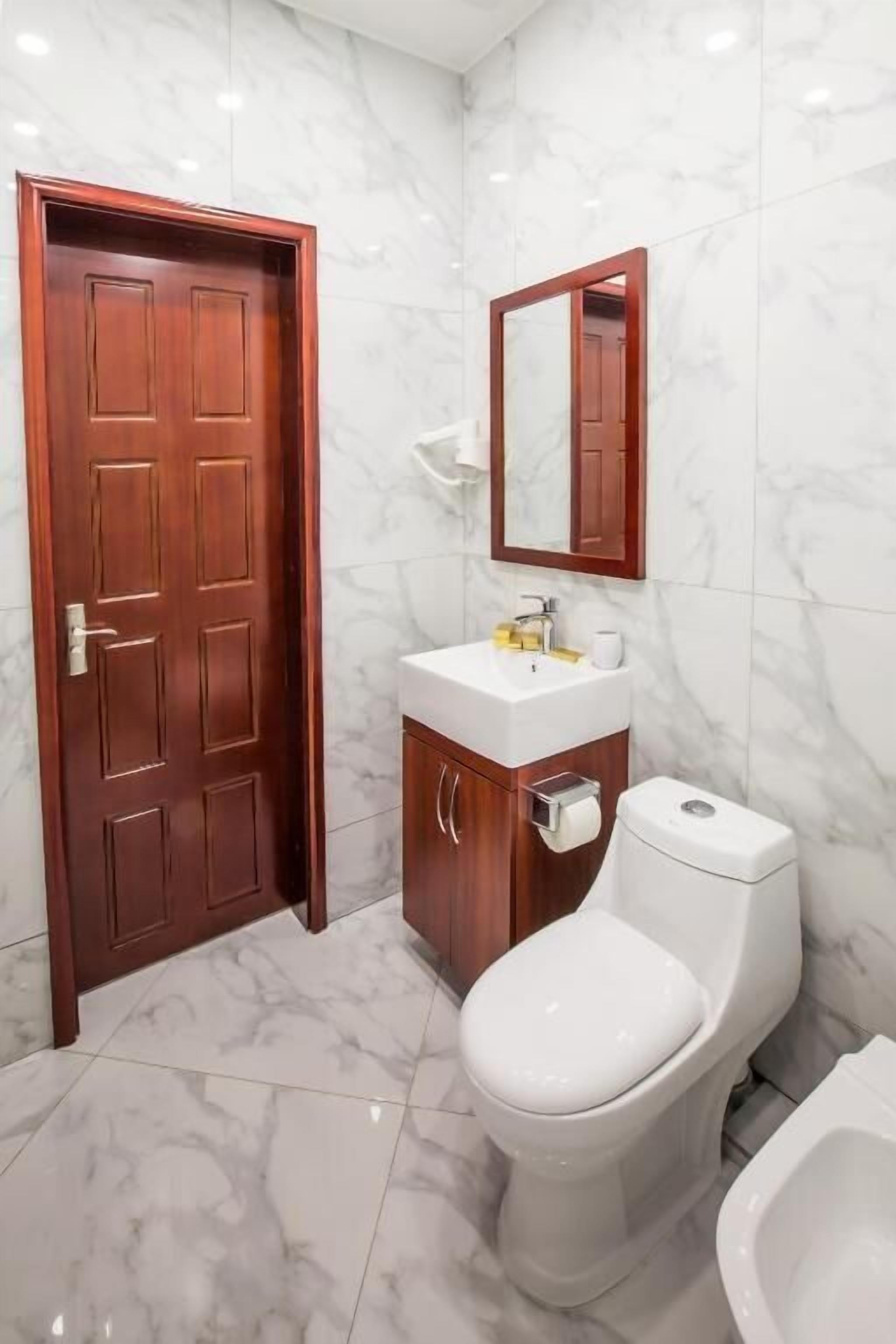 A bathroom with a marble floor, a wooden door, a white sink, a mirror, and a toilet.