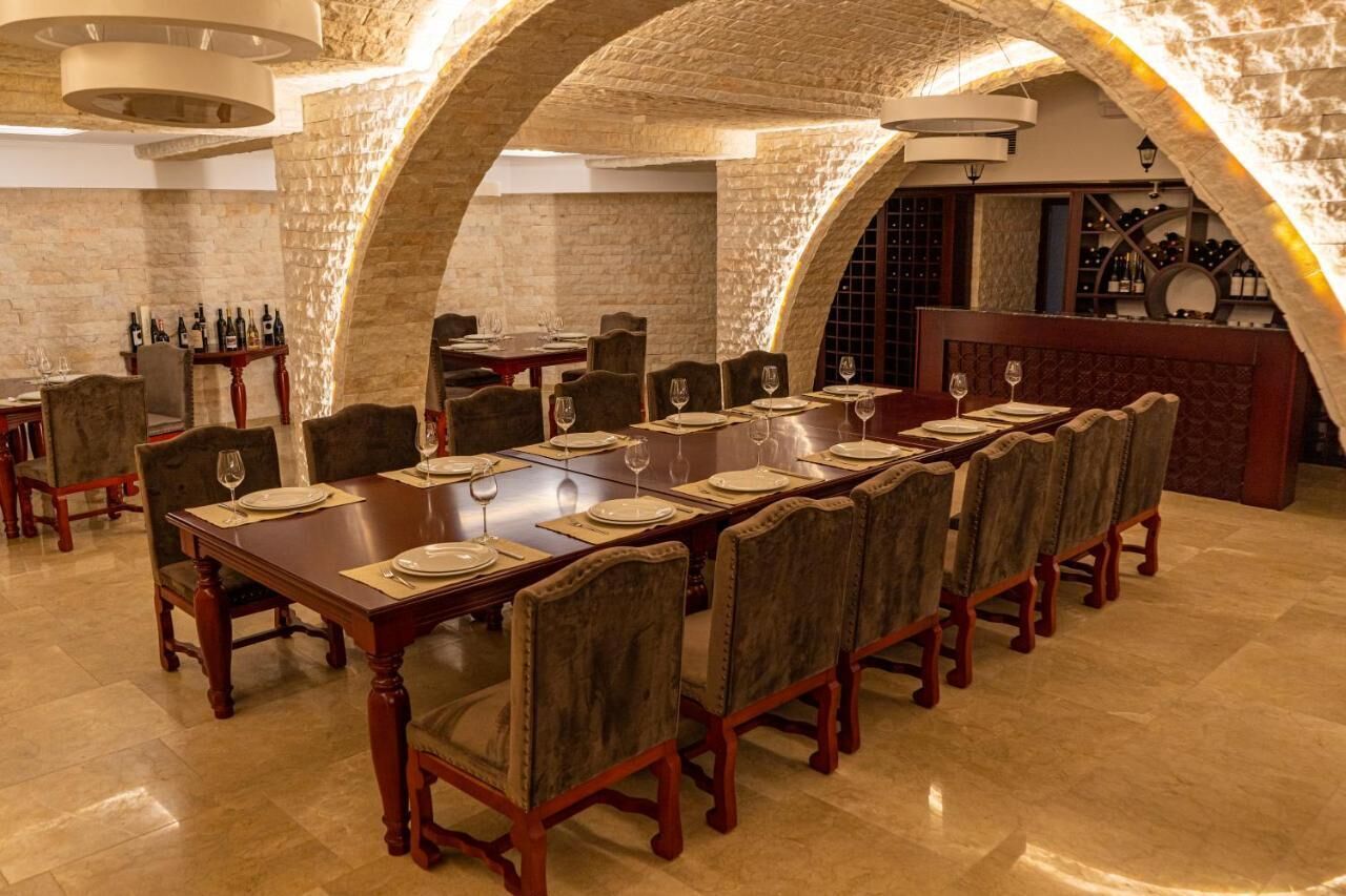 Un coin repas avec une longue table dressée pour le repas, entouré de murs en pierre et agrémenté, au fond, d’un meuble à vin.