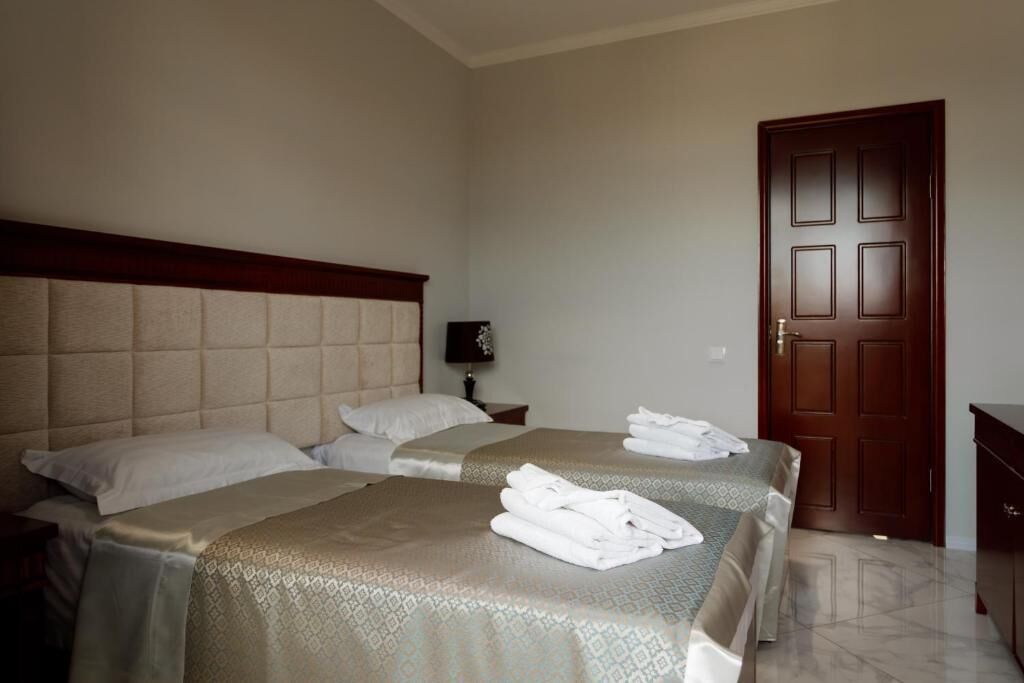 A hotel room with two beds, a wooden headboard, a nightstand with a lamp, and a door.