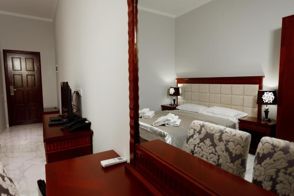 A hotel room with a bed, bedside tables, a desk, a chair, and a mirror.