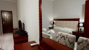 A hotel room with a bed, bedside tables, a desk, a chair, and a mirror.
