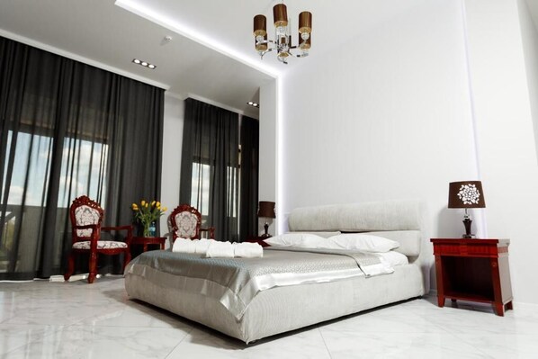 A modern bedroom with a large bed, a chandelier, a nightstand, and a chair.