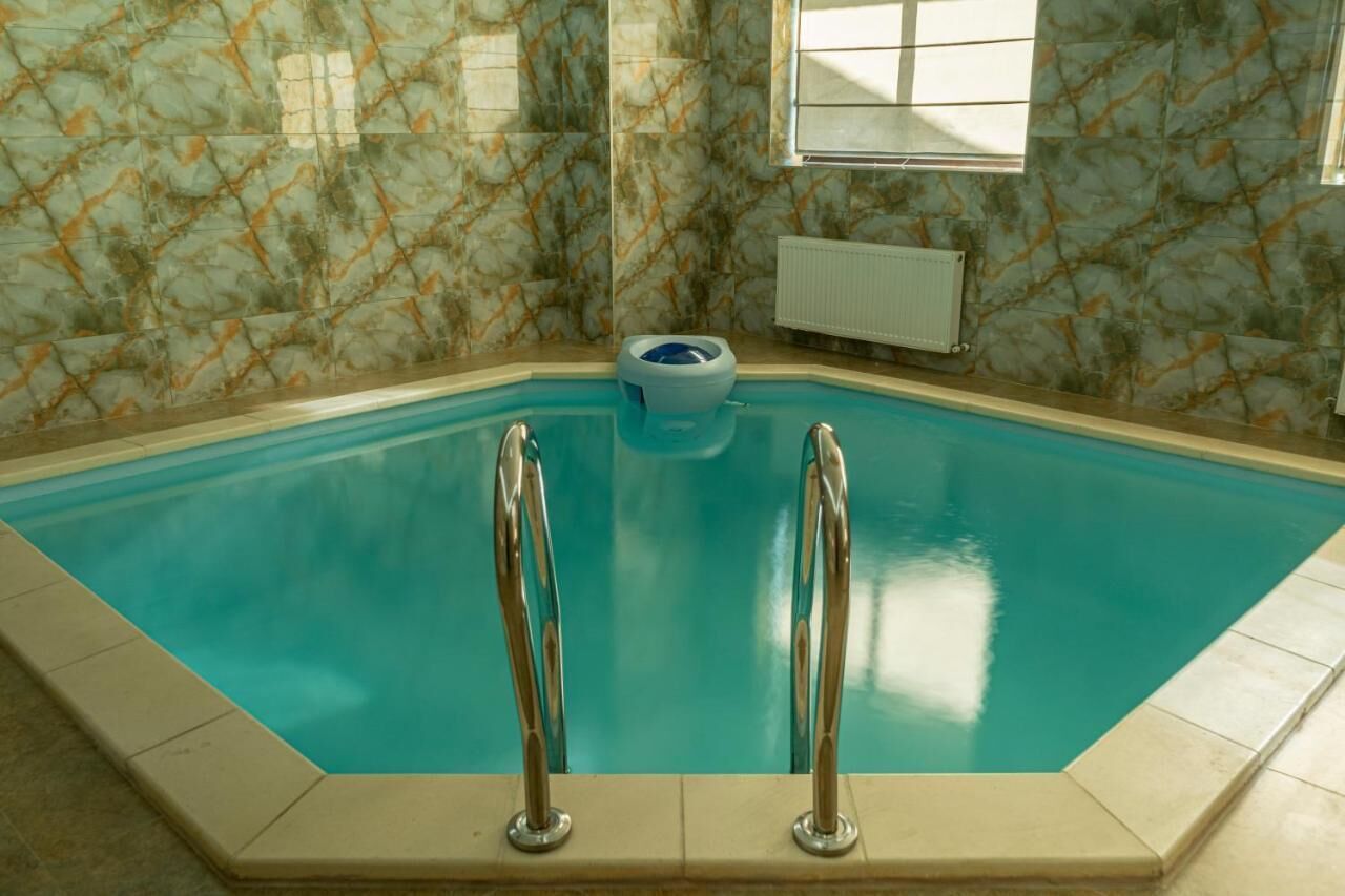 Una piscina techada con piso y paredes de azulejos azules, dos escaleras metálicas y un inodoro azul en el centro.