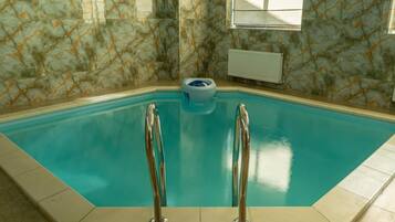 Una piscina techada con piso y paredes de azulejos azules, dos escaleras metálicas y un inodoro azul en el centro.