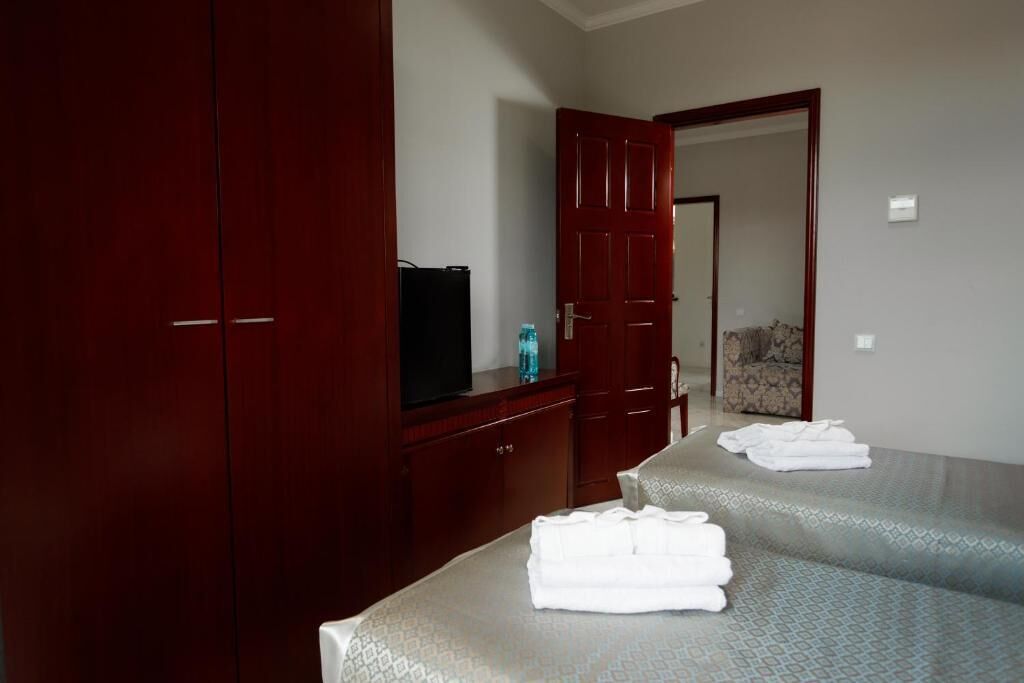 Quarto de hotel com um guarda-roupa espaçoso, televisão e duas camas com toalhas.