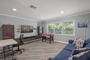 A modern living room with a flat-screen TV, a foosball table, a blue couch, and a dining table with chairs. - Sarasota Oasis: Pool, Game Room & Walk to Dining (Sarasota)
