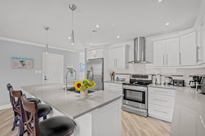 A modern kitchen with white cabinetry, stainless steel appliances, and a central island with bar stools.
