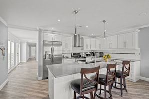 A modern kitchen with white cabinetry, stainless steel appliances, and a central island with bar stools.