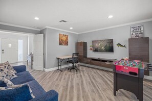 A living room with a foosball table, a sofa, a desk, and a television. - Sarasota Oasis: Pool, Game Room & Walk to Dining (Sarasota)