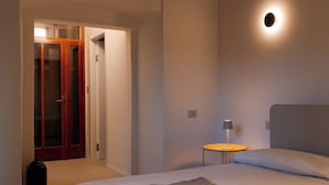 A bedroom with a large bed, a bedside table with a lamp, a wooden ceiling, and a door leading to a closet.