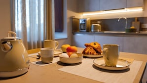 A breakfast setup with a kettle, cups, eggs, fruit, and croissants on a table.