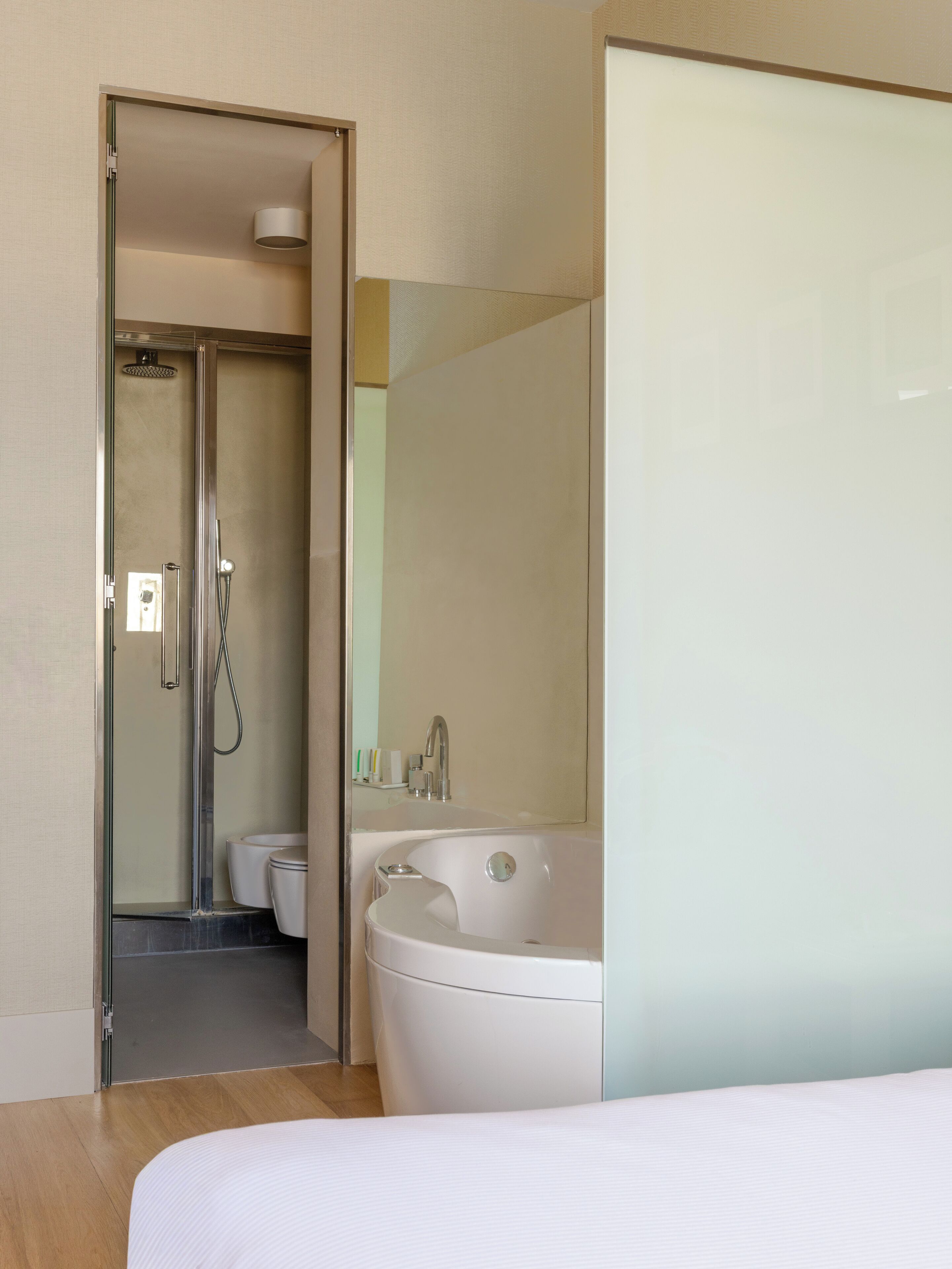 A modern bathroom with a glass-enclosed shower, a freestanding bathtub, and a mirror reflecting the room.