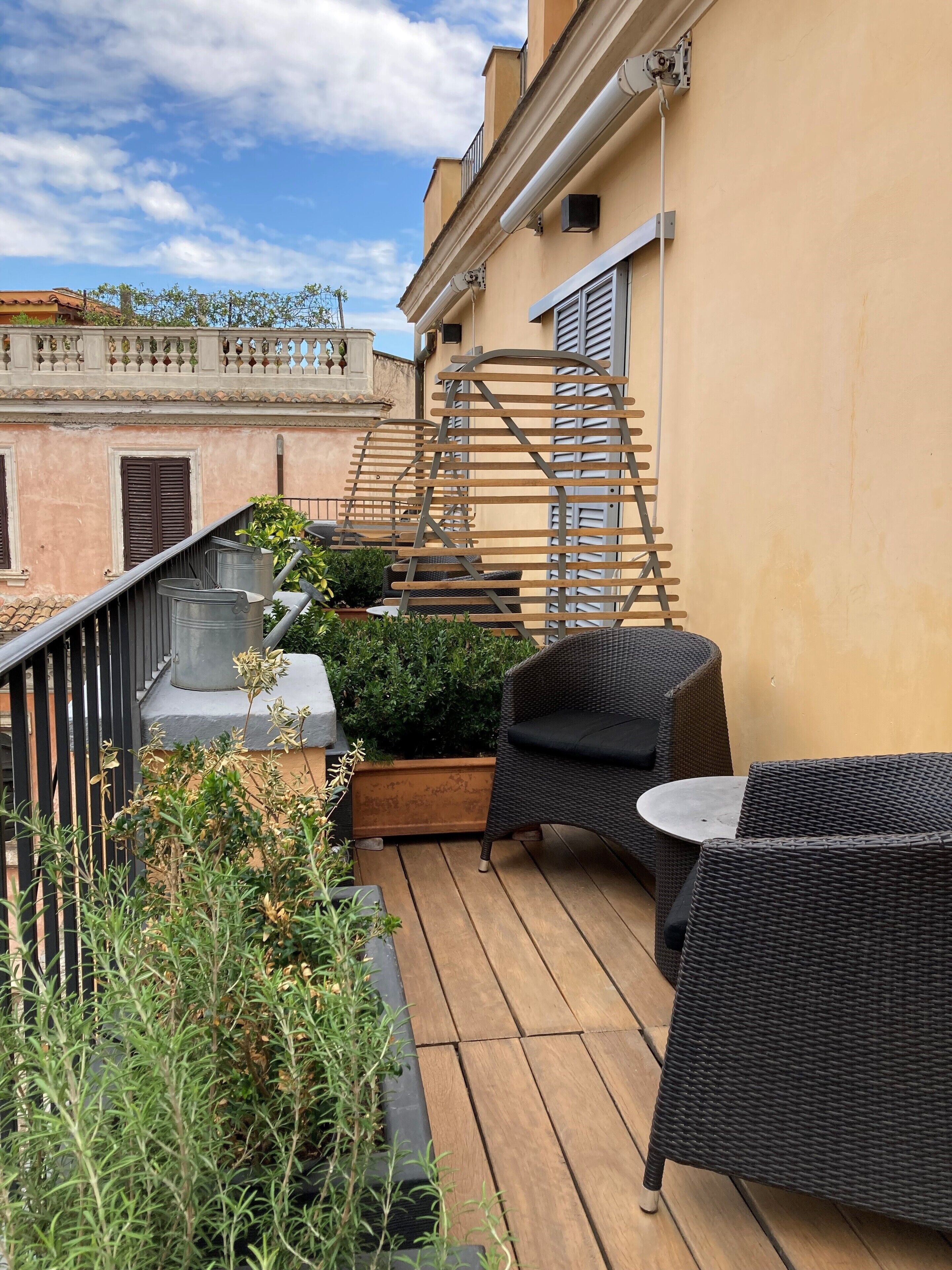 A rooftop terrace with wicker furniture, a small table, and a planter with greenery.
