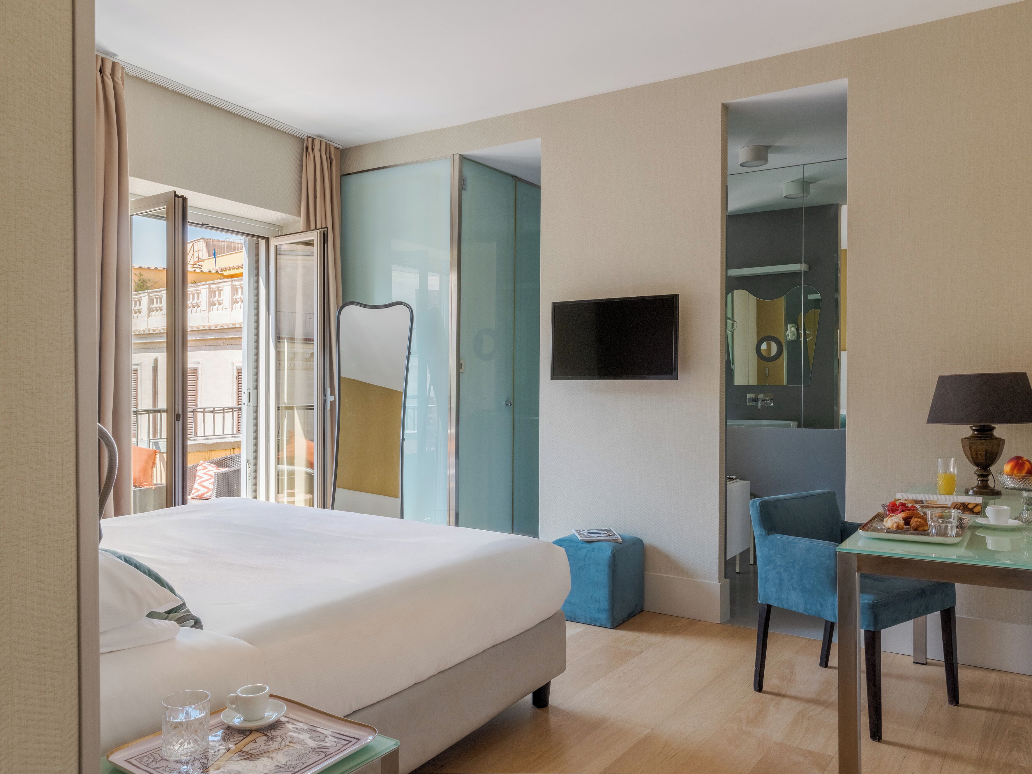 A hotel room with a bed, a desk with a lamp, a chair, a television, and a view of the outside.