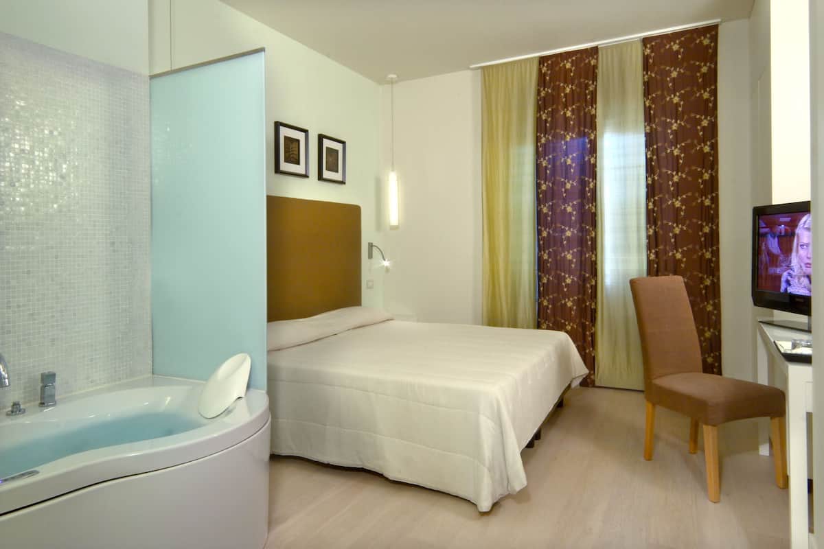Habitación de hotel con cama, una silla, escritorio con televisor y bañera.