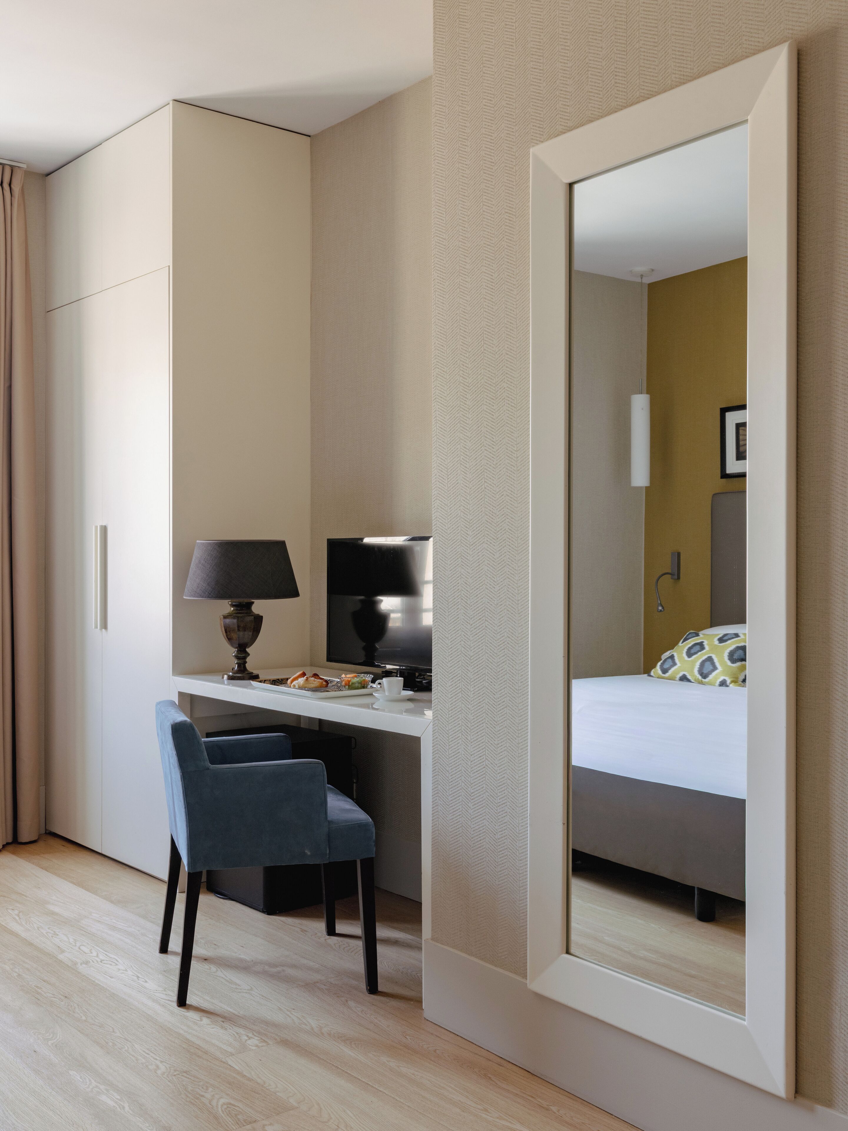 A hotel room with a bed, a desk with a chair, a television, and a mirror.