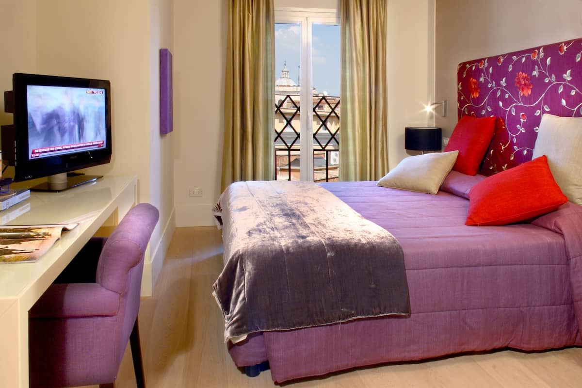 Un dormitorio con una cama, un escritorio con computadora y una ventana con cortinas.