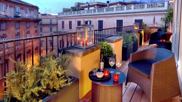 Une terrasse sur le toit, aménagée avec des meubles en osier, des plantes en pot et une table dressée avec des verres à vin et des bougies.