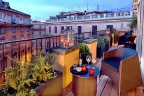 A rooftop terrace with wicker furniture, potted plants, and a table set with wine glasses and candles. - Domus Adriani (Rome)