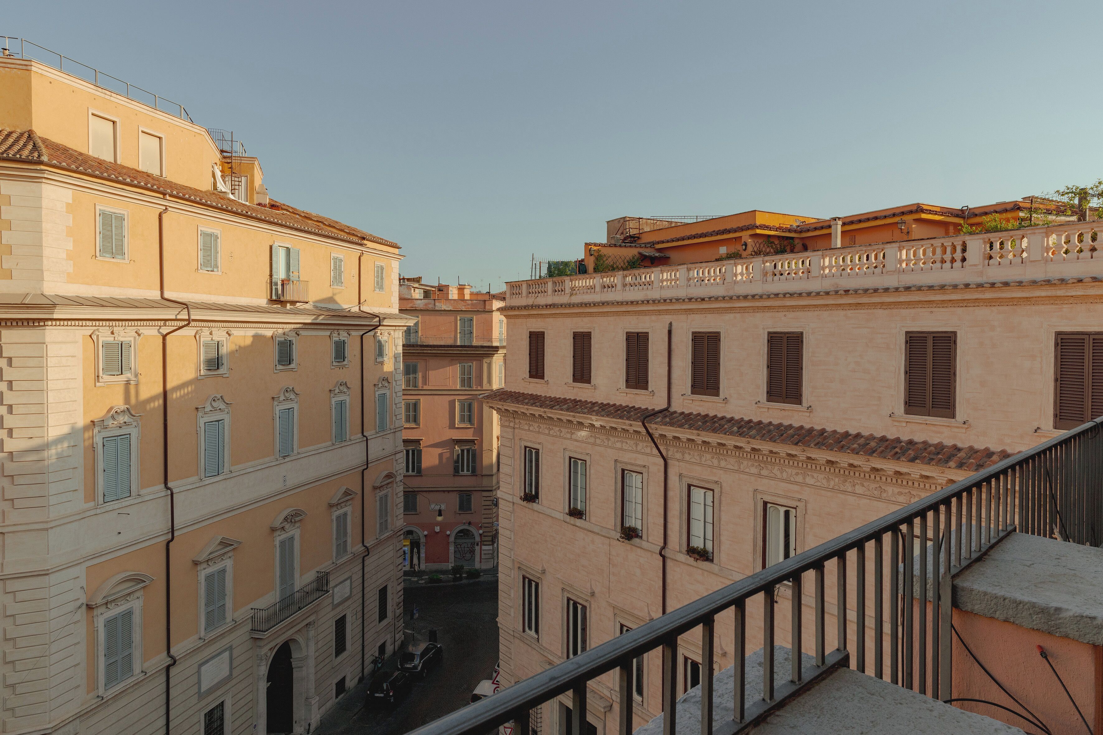 A narrow street between buildings with balconies and windows, a clear sky, and a metal railing on the right.