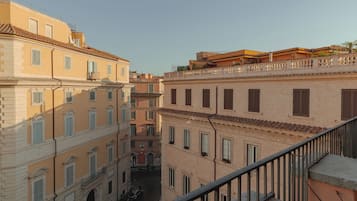 A narrow street between buildings with balconies and windows, a clear sky, and a metal railing on the right.