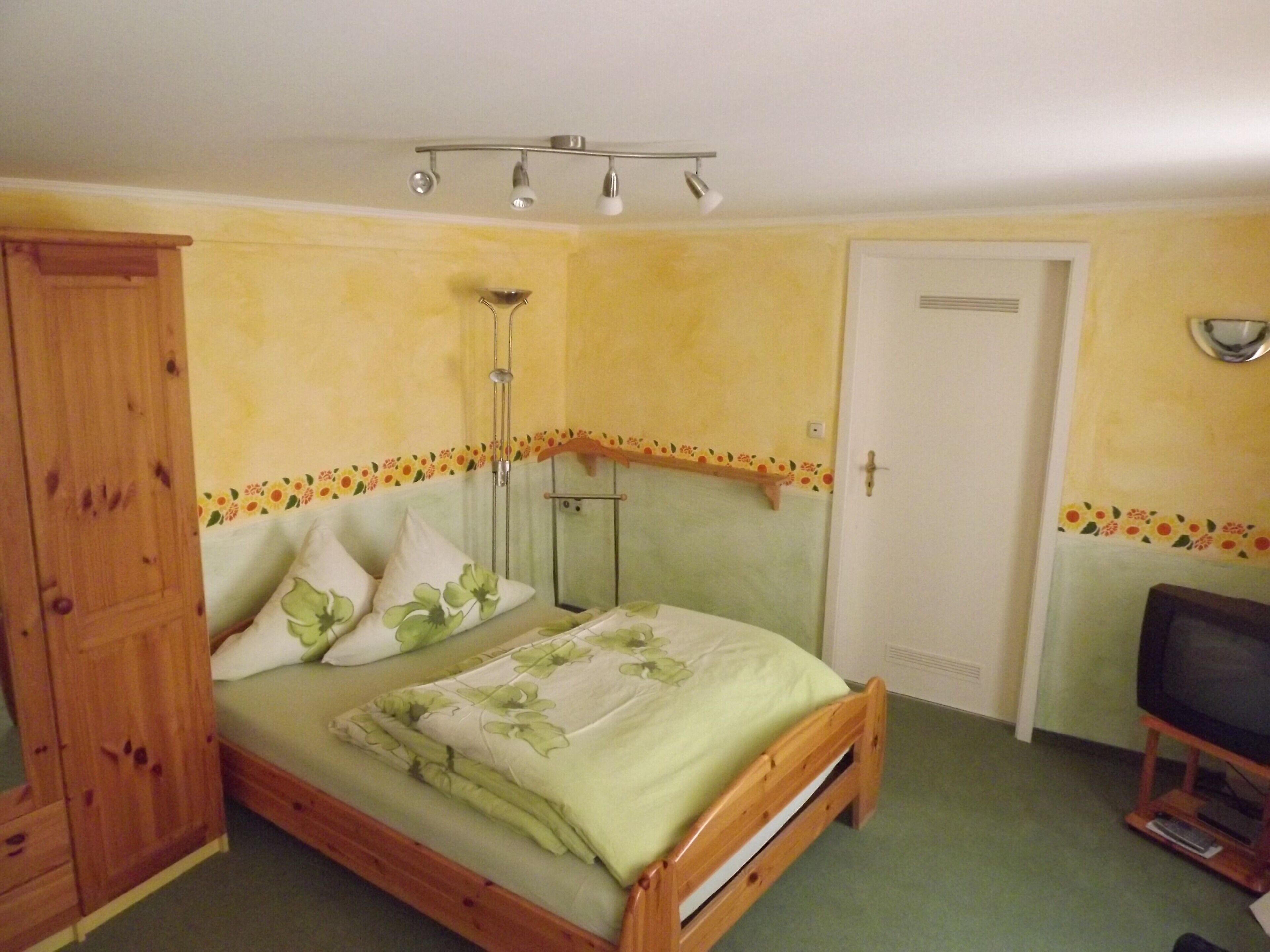Une chambre à coucher avec un lit, une armoire en bois, une télévision et une porte.