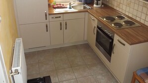 Een kleine keuken met een magnetron, kookplaat, spoelbak en een radiator.