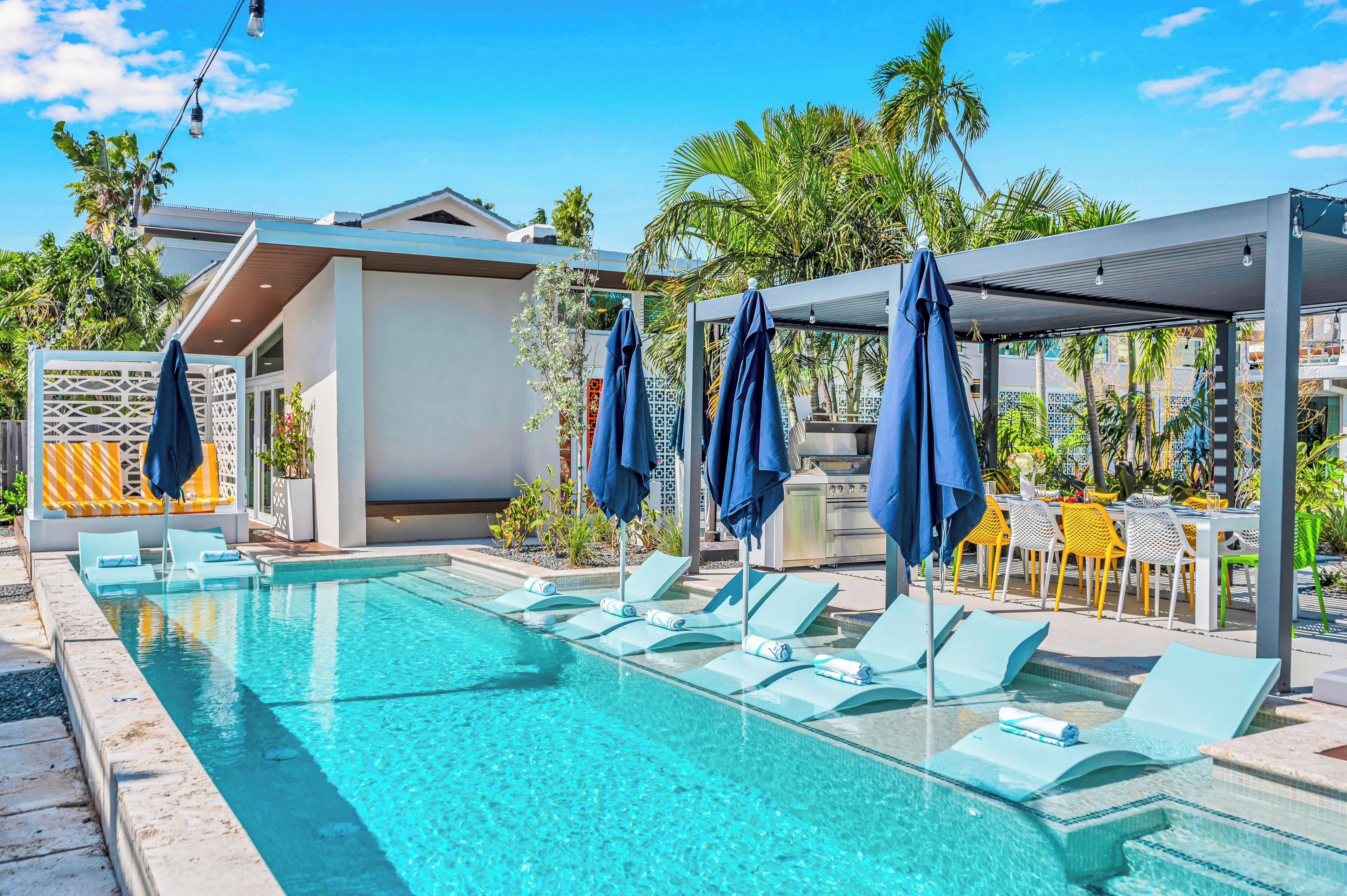 A pool area with lounge chairs and umbrellas, a covered seating area, and a building with a modern design.