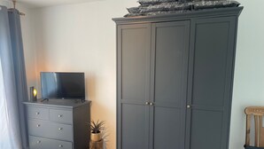 Ett rum med en mörk garderob, en tv på ett skåp, en trästol och en liten växt.