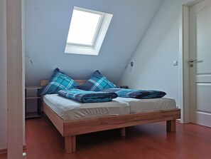 A single bed with a wooden frame, a skylight, and a bedside table with a lamp.
