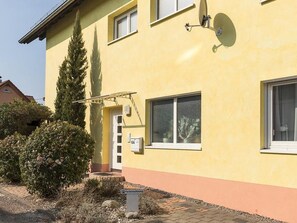 A yellow building with a satellite dish, a window with a screen, and a door with a mailbox.