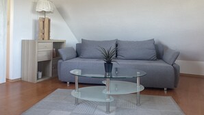 Una sala moderna con un sofá gris, una mesa de centro de vidrio y un armario de madera.