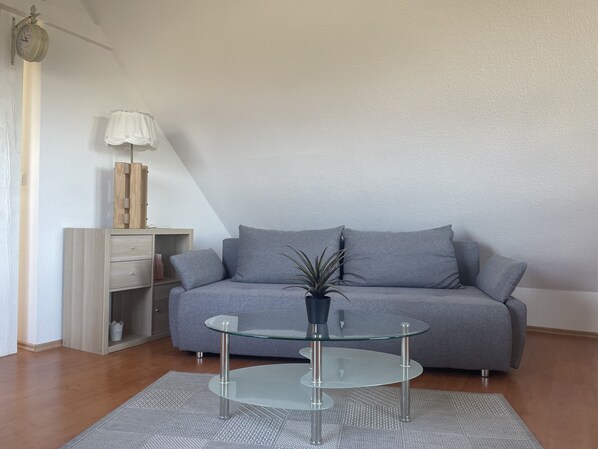 A modern living room with a grey sofa, a glass coffee table, and a wooden cabinet.