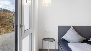 A modern room with a large window, a round table, a grey sofa with pillows, and a wall-mounted light fixture. - Room '5' with Shared Terrace and Wi-Fi (Dußlingen)