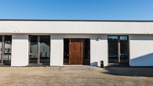 A modern building with a large wooden door, large windows, and a gravel driveway. - Room '5' with Shared Terrace and Wi-Fi (Dußlingen)