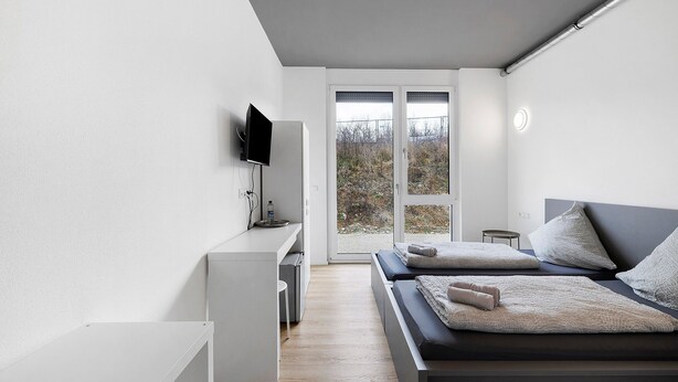 A modern bedroom with a bed, a TV, a desk, and a view through a glass door. - Room '5' with Shared Terrace and Wi-Fi (Dußlingen)
