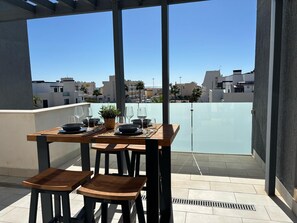 Un coin repas avec une table dressée pour quatre personnes, une plante en pot et une vue sur le paysage urbain.