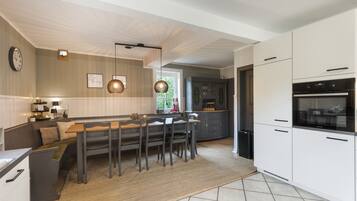 A modern kitchen with a dining area, featuring a built-in oven, a large island with seating, and a clock on the wall.
