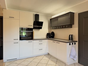 A modern kitchen with white cabinetry, a built-in oven, a coffee maker, and a kettle.