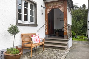 Un banco de madera con cojín frente a un edificio de fachada blanca y puerta de madera con la inscripción 'Anno 1832'.